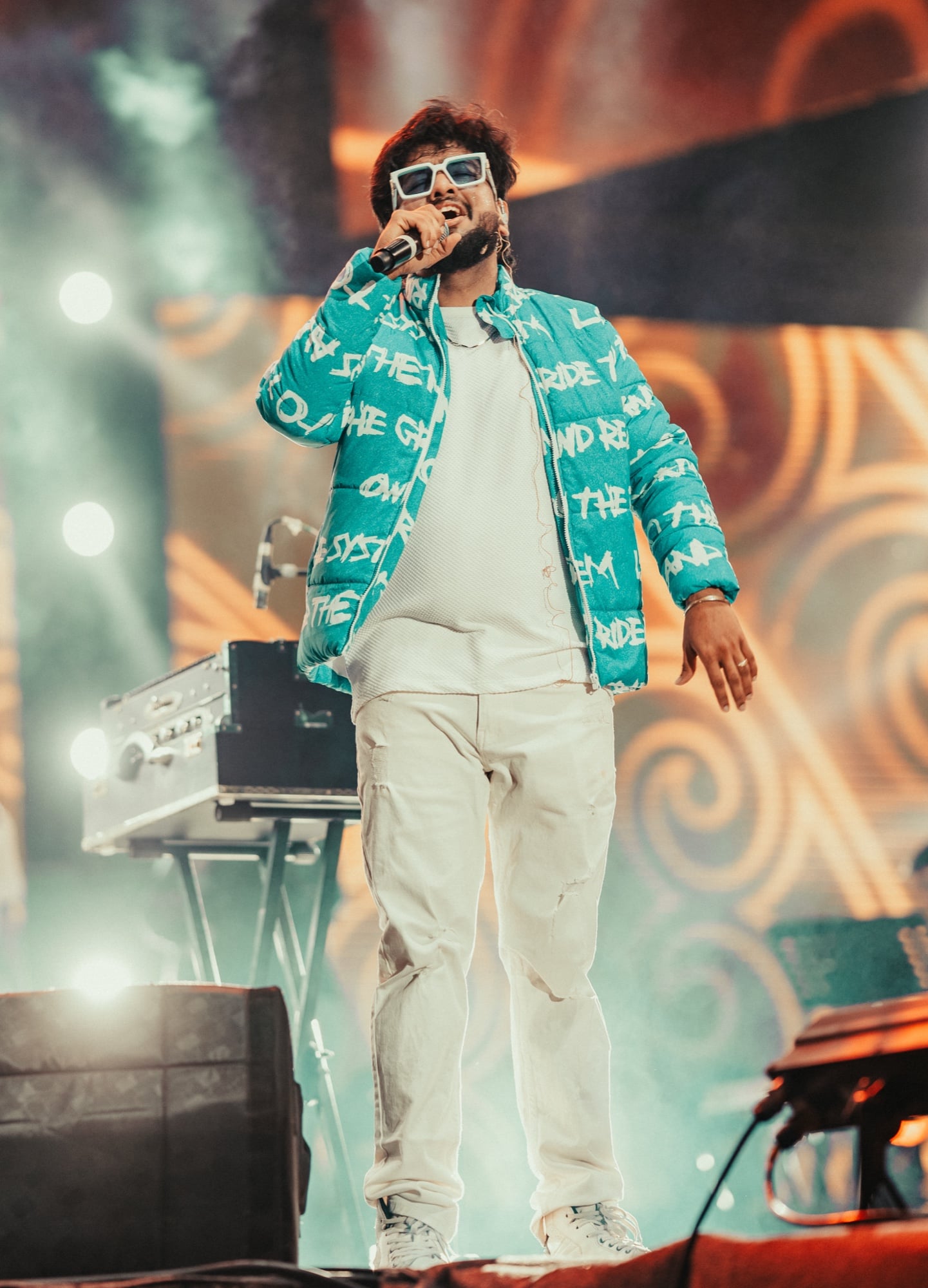 Monk singing on stage in a teal graffiti-print jacket and white sunglasses