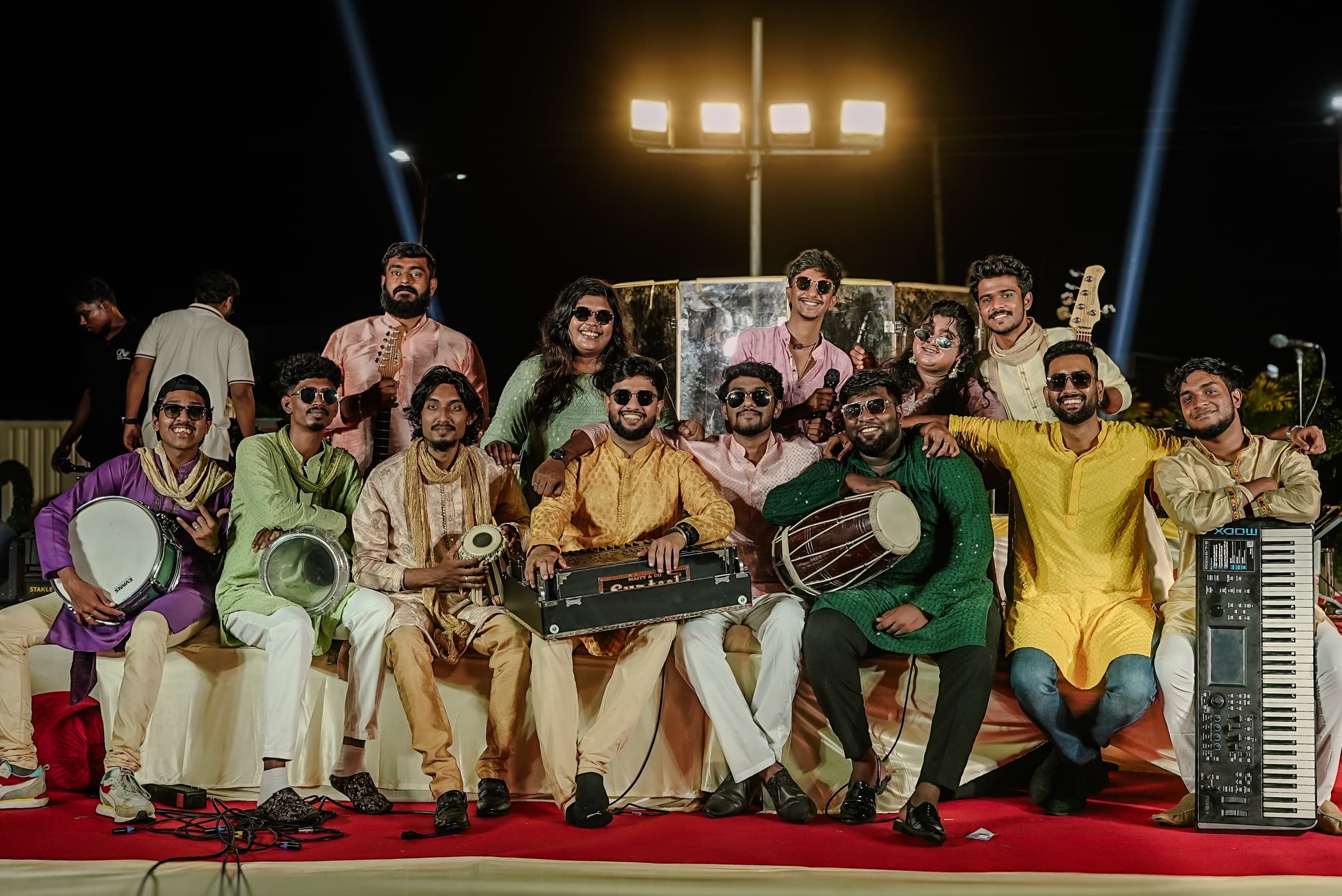 The Office Gaana band posing on stage in festive kurtas with harmonium, tabla, dholak, drums and keys